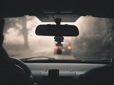 The view through a windshield on a misty road, with the rear-view mirror and the unit behind it