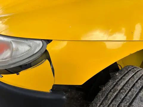 The front corner of a yellow car, its bumper cover cracked by the headlight